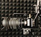 A close-up overhead view of a professional camera setup with a large lens and various accessories on a textured black surface.